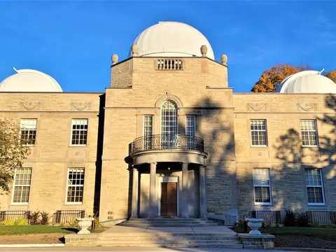 The sandstone David Dunlap Observatory building in Richmond Hill, topped by three white telescope domes and glowing in autumn sunshine under a clear blue sky