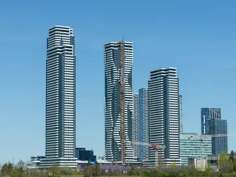 Tall white-and-glass condo towers of the Vaughan Metropolitan Centre against a clear blue sky, with green trees in the foreground